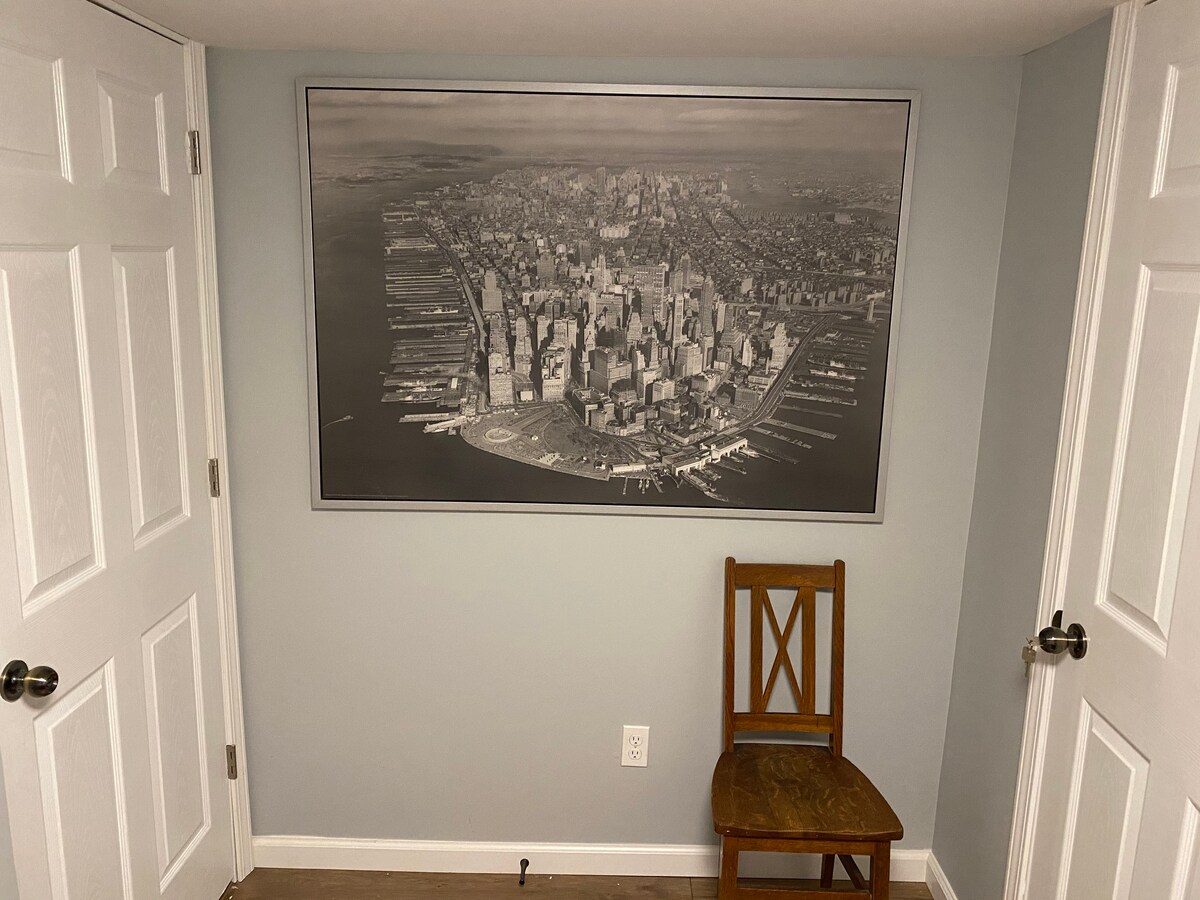 A corner of the room features a vintage-style wooden chair, positioned below a large black-and-white aerial photograph of a city skyline. The walls are painted in a soft blue hue, and two white doors are visible, adding to the elegant simplicity of the space.