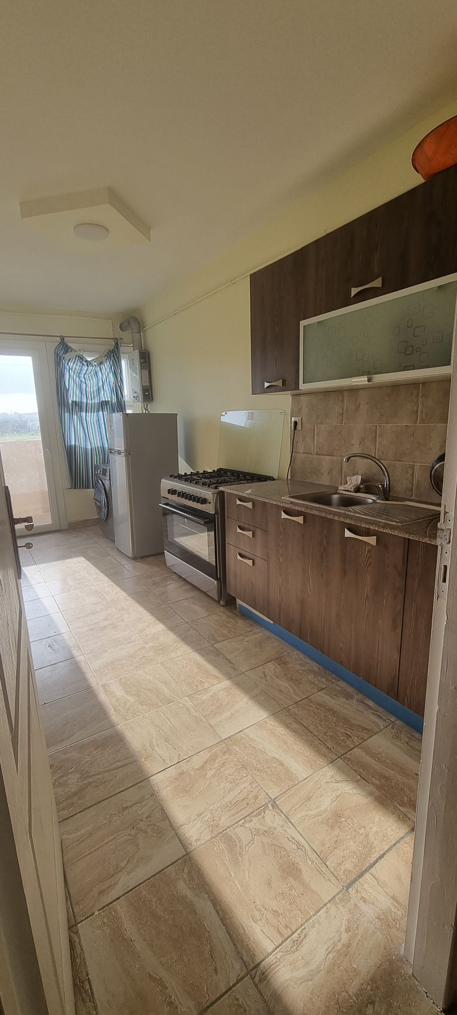A well-equipped kitchen is presented with dark wood cabinets and stainless steel appliances. A large window allows natural light to fill the space, illuminating the countertops. A stove and dual sinks are positioned along one wall, while a refrigerator stands against the opposite side.