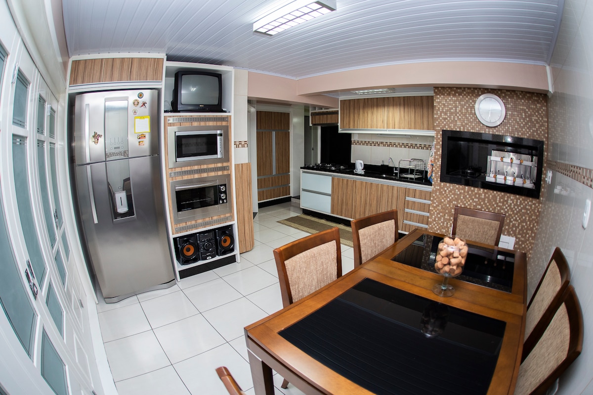 A well-equipped kitchen is presented with modern appliances, including a refrigerator, microwave, and oven. A wooden dining table accommodates six and is centered in the space. Natural light enters through large windows, highlighting the clean lines and neutral colors of the cabinetry.