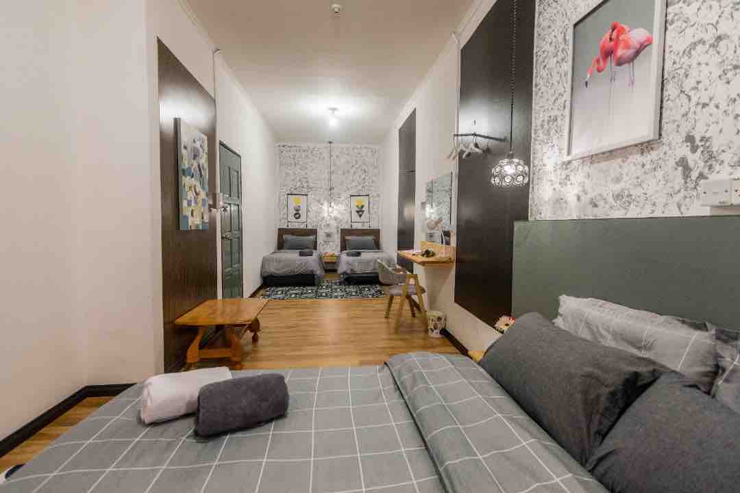 A spacious room is shown, featuring two separate beds and a cozy sleeping area. The walls are decorated with subtle patterns, and a bright piece of artwork adds a touch of color. Natural light enters through a window, illuminating the wooden floor.