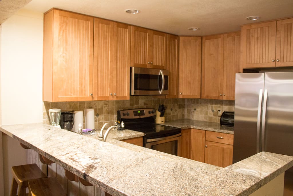 Full kitchen with stainless steel appliances and bar stools.
