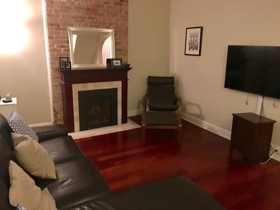 Cozy living room with exposed brick, working gas fireplace, flat screen HD TV, and comfy leather couch.