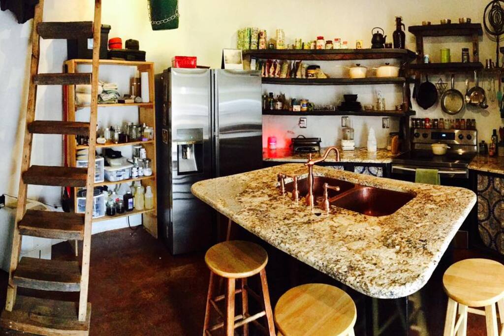 Lower level offers a kitchen with new fridge and electric range stove, granite counters, copper sink, bar stools, pots and pans, dishes, utensils and shelf space for your food and personal items. The shower and a rocket wood-burning stove are to the left of this shot.
