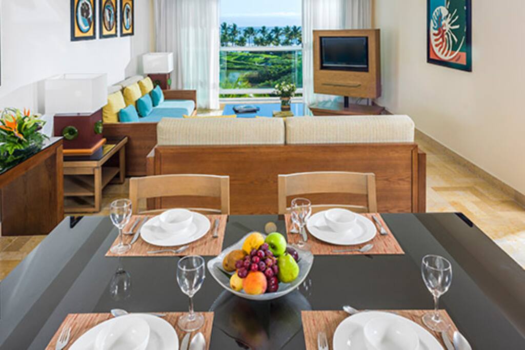 The One Bedroom Suite features one bedroom with a king-size bed, one bathroom, a living room with dining table and kitchen, a balcony, and two TVs.