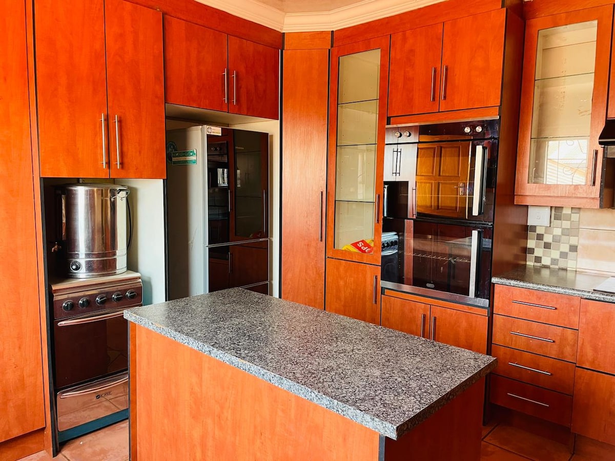 A modern kitchen features wooden cabinetry with sleek hardware. A central island is topped with a grey countertop, and built-in appliances are visible, including an oven and a refrigerator. The layout is practical, allowing for easy movement and organization.
