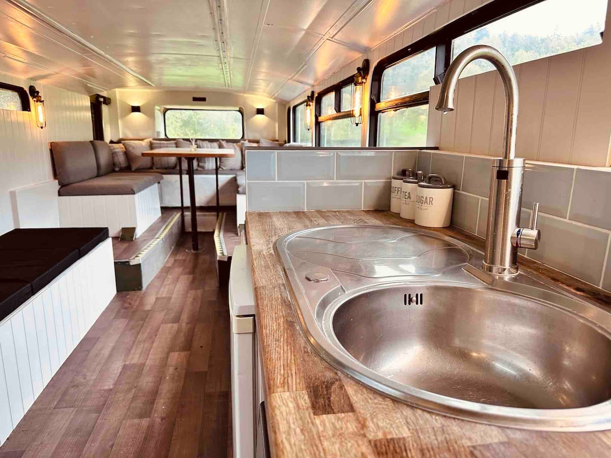 An inviting interior features a well-equipped kitchen area with a double sink and wooden countertops. Natural light filters through several windows, enhancing the spacious feel. A cozy dining table and seating area are visible, creating a comfortable gathering space for guests.