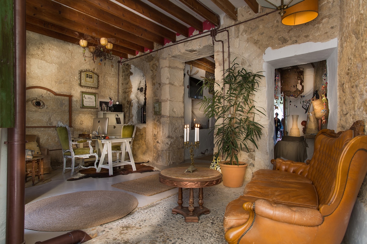 The inviting living area features a rustic stone wall and wooden beams supporting the ceiling. A plush orange sofa and a round coffee table create a cozy seating arrangement. A decorative plant adds a touch of nature, while soft lighting enhances the space's warm ambiance.