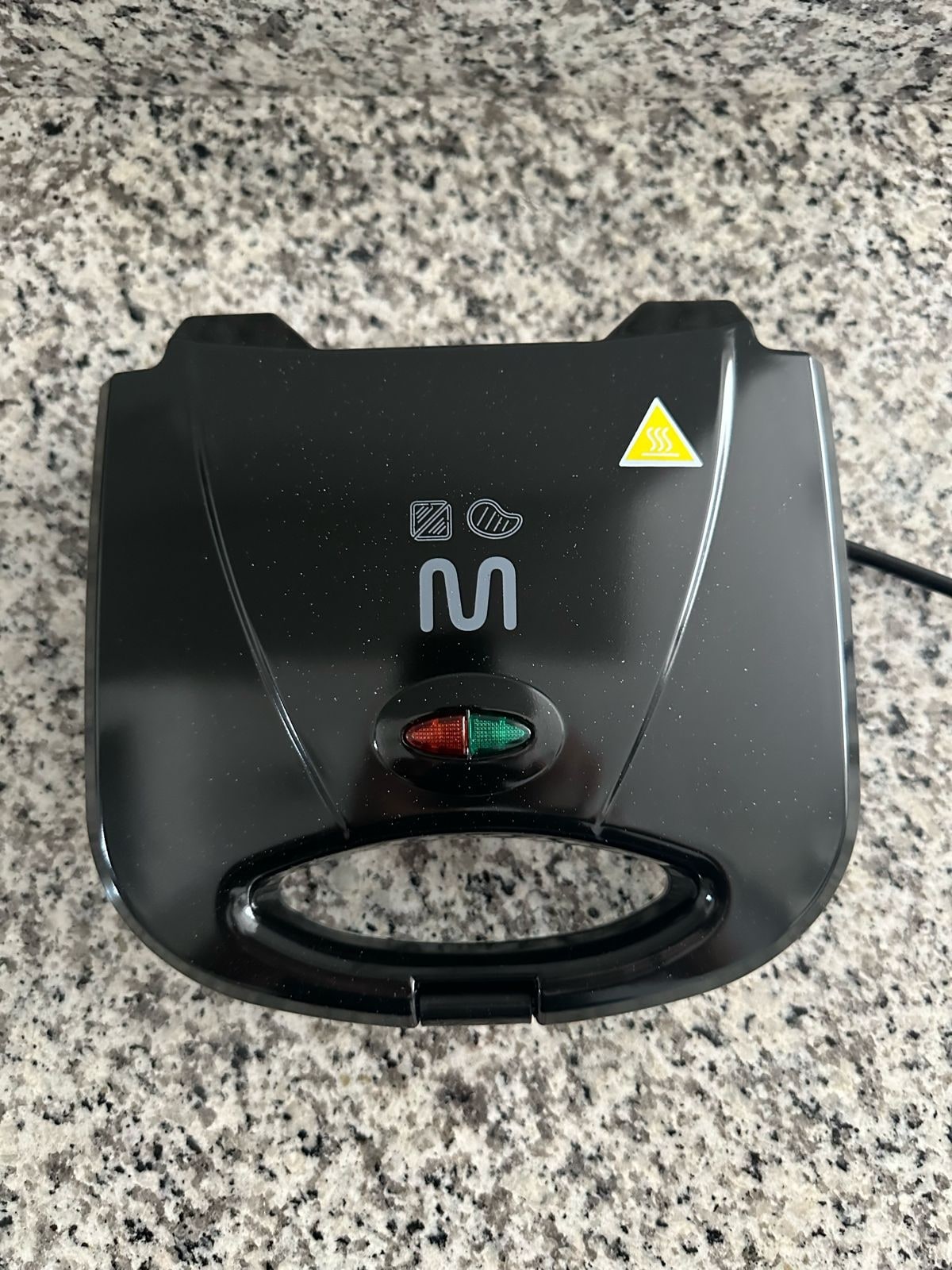 A compact kitchen appliance is displayed on a speckled granite countertop. Its sleek, black exterior features a prominent handle and indicator lights, indicating operational status. The appliance appears to be suitable for various cooking tasks.
