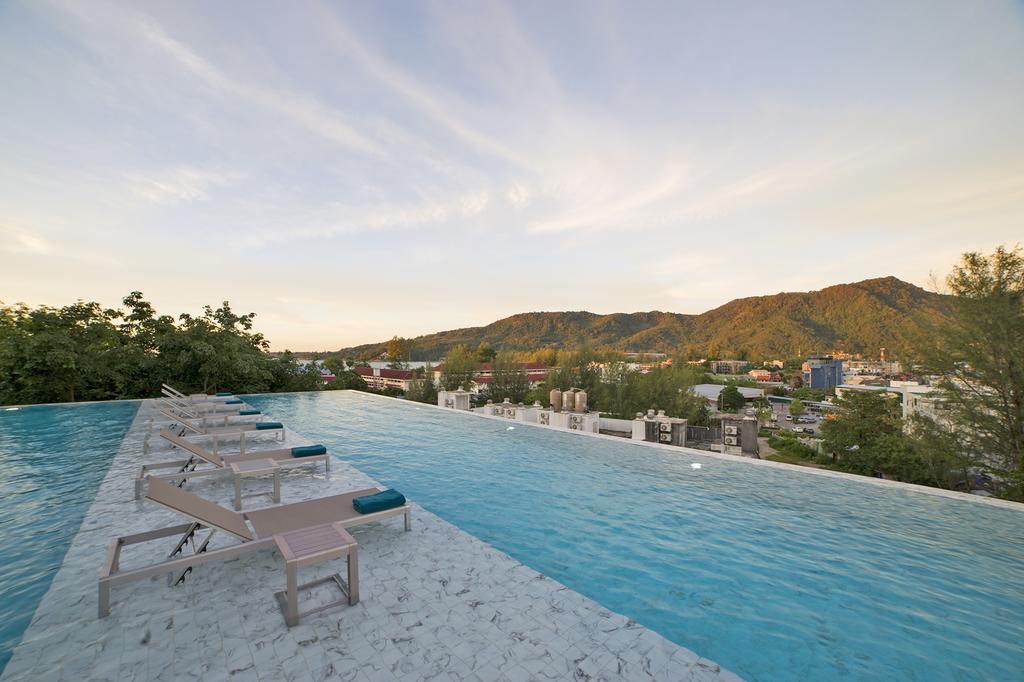 An infinity pool extends along a marble deck, offering unobstructed views of surrounding mountains and the charming landscape below. Several sun loungers are positioned alongside the pool, inviting relaxation under the open sky. The scene captures the serene ambiance of the outdoor space.