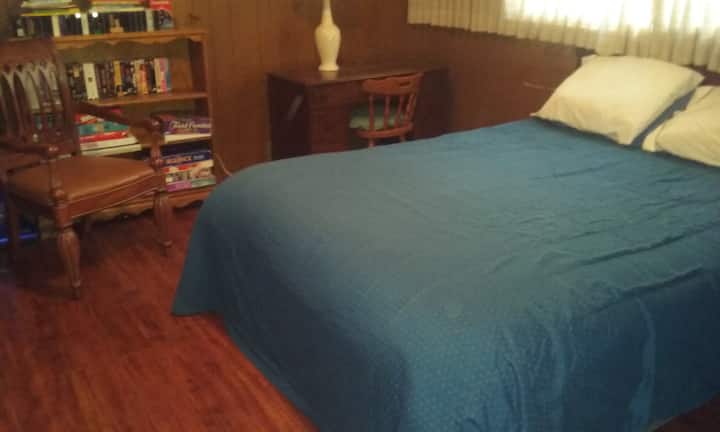 Queensize bed, bureau, bordspellen en VHS-films, ladekast (niet zichtbaar), tv (niet zichtbaar)