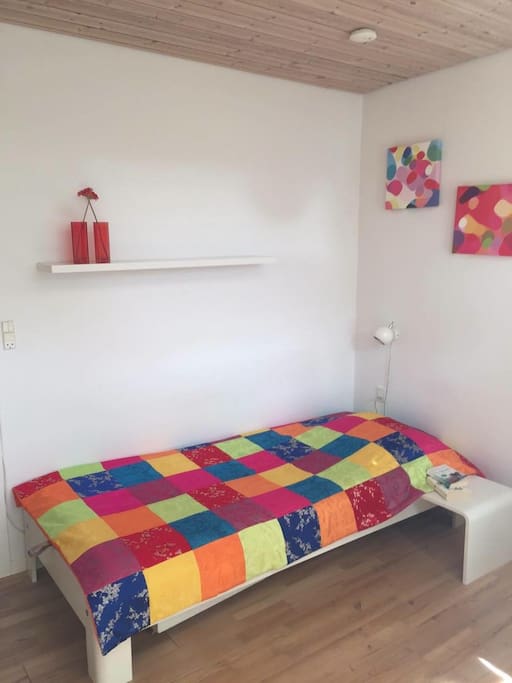 The bed in the room. Includes night lamp, night stand and a shelf above.