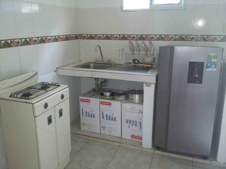 ZONA DE COCINA COMPARTIDA CON ESTUFA, NEVERA Y UTENCILIOS DE COCINA.