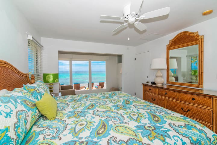 Une chambre de maître luxueuse avec un lit king-size vêtu de draps impeccables, une vue sur l'océan et un ventilateur de plafond pour plus de confort. Des couleurs douces et apaisantes et une lumière naturelle abondante font de cette pièce une retraite paisible.