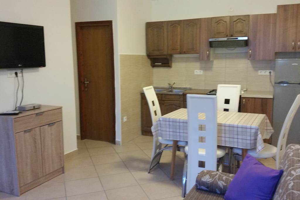 Fully equipped kitchen with living room. In kitchen is dining table. In living room is tv and a sofa for two.