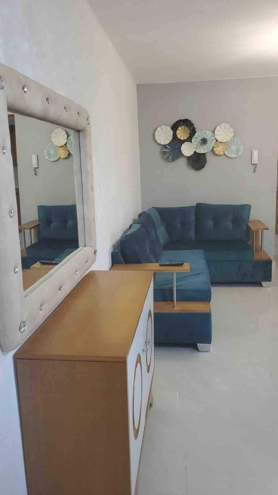 A welcoming living area features a plush blue sectional sofa, complemented by a wooden side table. A decorative mirror adds depth to the space, while a wall display of circular art pieces in soft colors provides an inviting focal point.