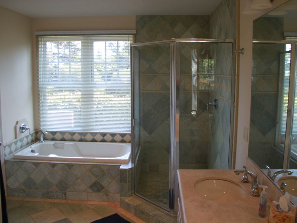 A spacious bathroom features a large soaking tub adjacent to a glass-enclosed shower. Natural light filters through the window, highlighting the tile backsplash and countertops. A mirrored vanity with dual sinks complements the overall design.