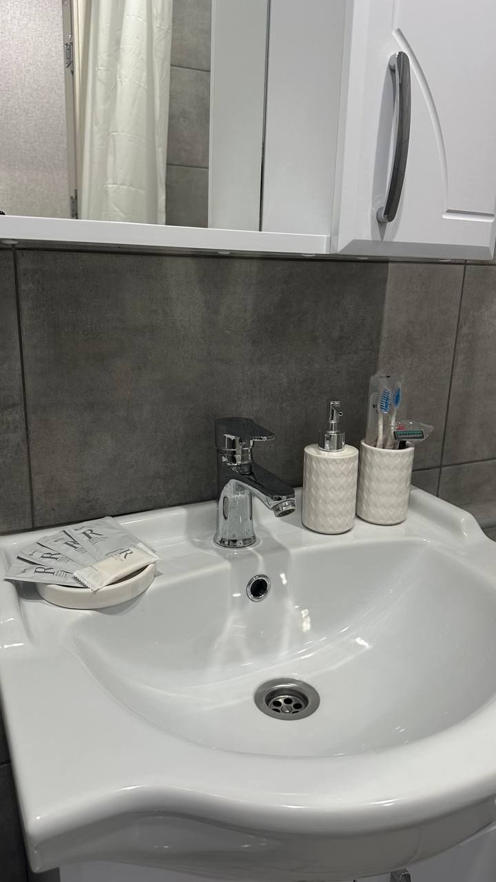 A clean bathroom sink area features a sleek faucet and round basin. Personal care items are organized neatly in matching holders. A small dish holds toiletries, and a reflective mirror enhances the space's brightness. Soft lighting contributes to a calm ambiance.