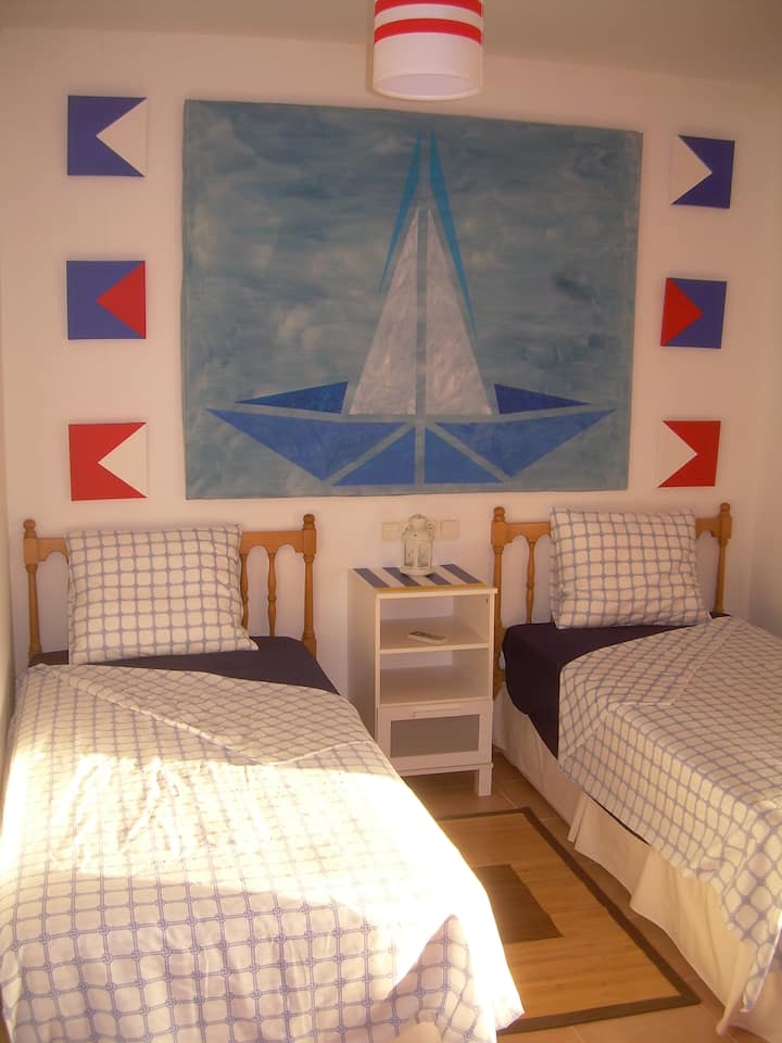 חדר שינה עם שתי מיטות וחלון רחב בחוץ.