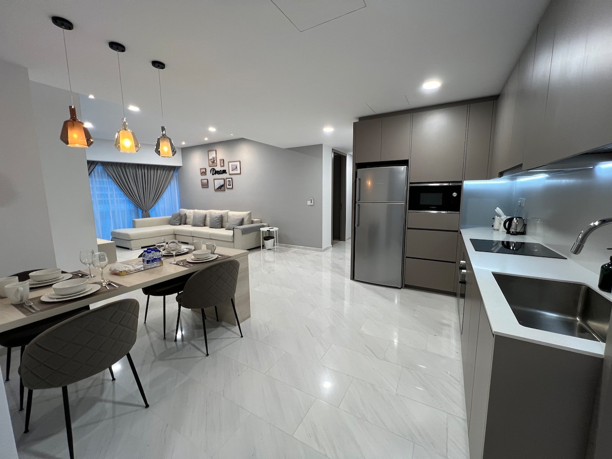 An open-concept kitchen and dining area is presented, featuring a modern kitchen with stainless steel appliances and a sleek countertop. A dining table with four chairs is set for a meal, and a comfortable living space with a large sectional sofa is visible in the background.