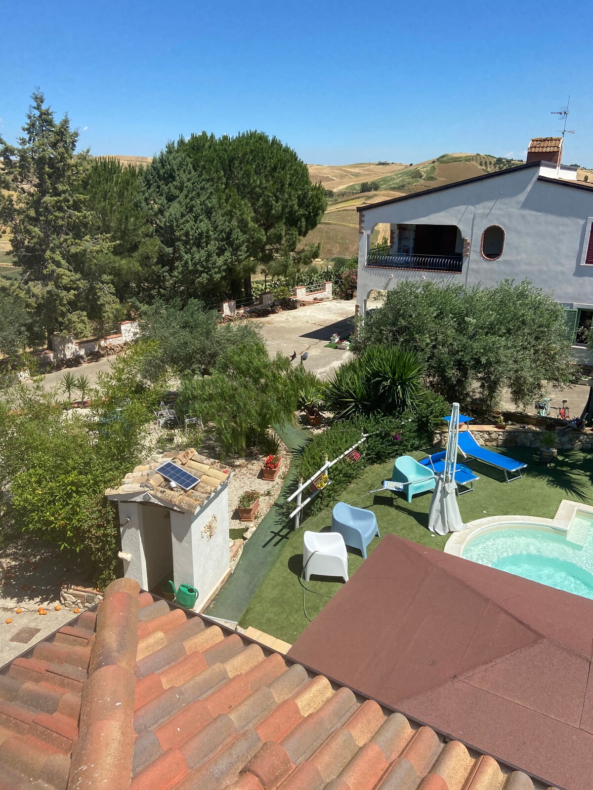 An aerial view reveals the outdoor space featuring a relaxing pool and shaded seating area. Lush greenery and trees provide natural surroundings, while a winding pathway leads through the garden, enhancing the tranquil atmosphere of the property.