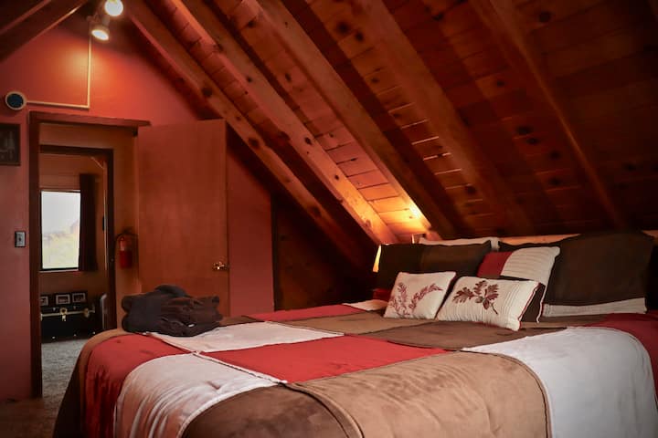 Bedroom #2: Upstairs master bedroom has a California king bed with hypoallergenic luxury bedding, custom log headboard, & rustic wood ceiling beams. It has a dresser, air conditioning unit, closet, new etched wood flooring, & grand mountain views.