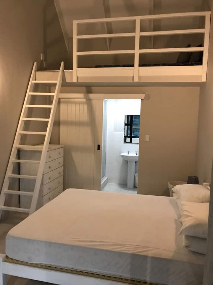 חדר שינה 1 (מקלחת צמודה), מיטה זוגית עם מזרן על הרצפה בחלל הלופט. החדר נפתח למסדרון המשותף.