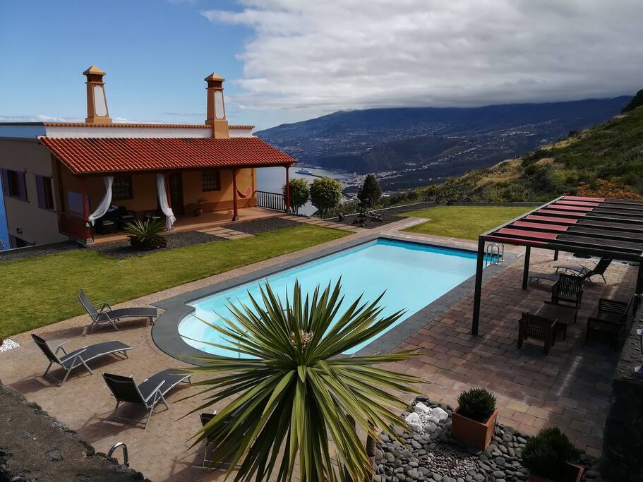 Zona de piscina y spa, dotada de pérgola con toldo, sillones, mesa y tumbonas.