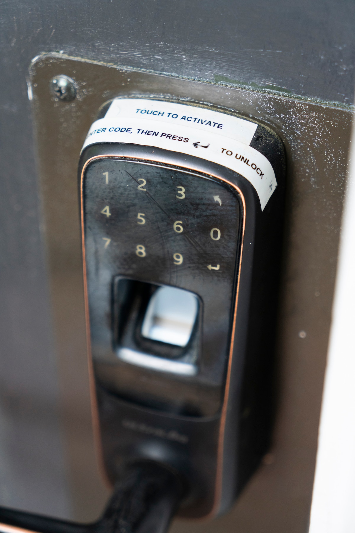 A close-up view of a digital keypad lock is shown on a door. The keypad features numbers and instructions for activation. The lock is mounted on a door frame, designed for secure access to the property.