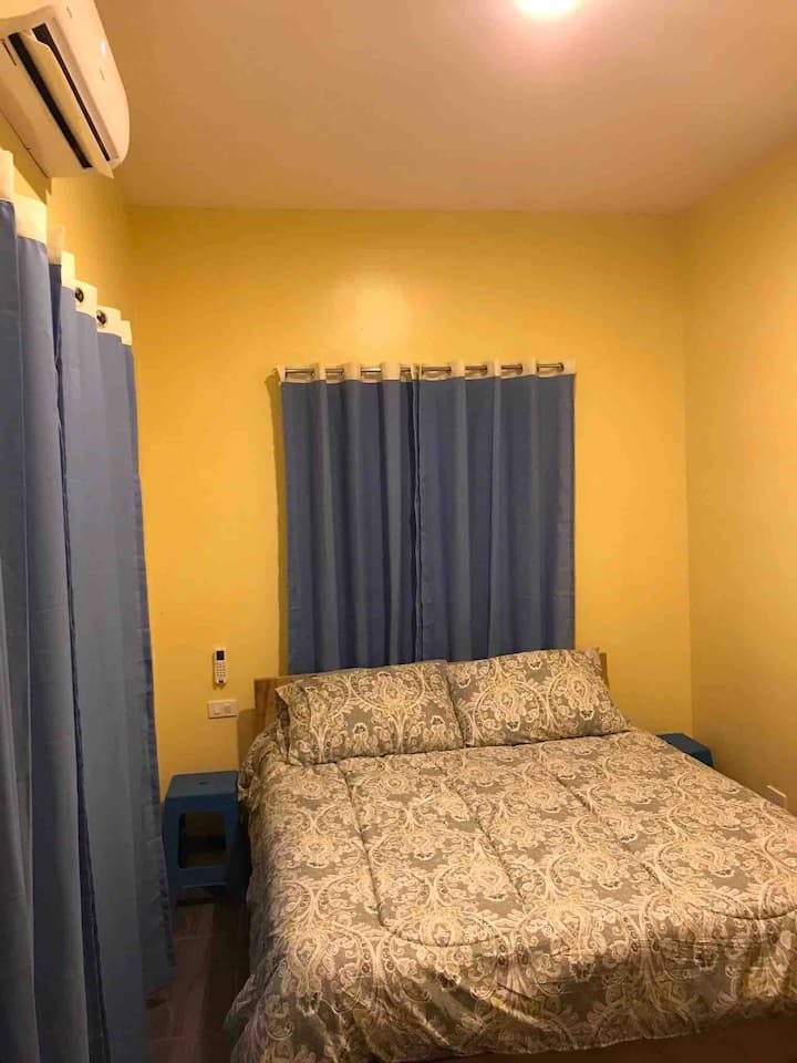 Bedroom with queen bed and split type air conditioner, window on the side over looking to the oceanfront and other window over looking towards main gate.