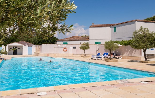 A spacious heated pool is surrounded by sun loungers and olive trees. The clear blue water reflects the bright sky and offers an inviting atmosphere. The pool area is well-maintained, with safety features visible along the perimeter.