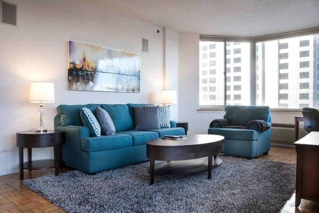 Comfortable living room with pullout sofa bed, club chair and over-sized windows providing a lot of natural light