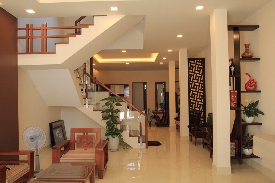 A spacious entryway is highlighted by a stylish staircase adorned with wooden railings. Natural light illuminates the polished floor, while potted plants and decorative elements enhance the welcoming ambiance. Seating areas are arranged for comfort, providing a glimpse into the thoughtfully designed living space.