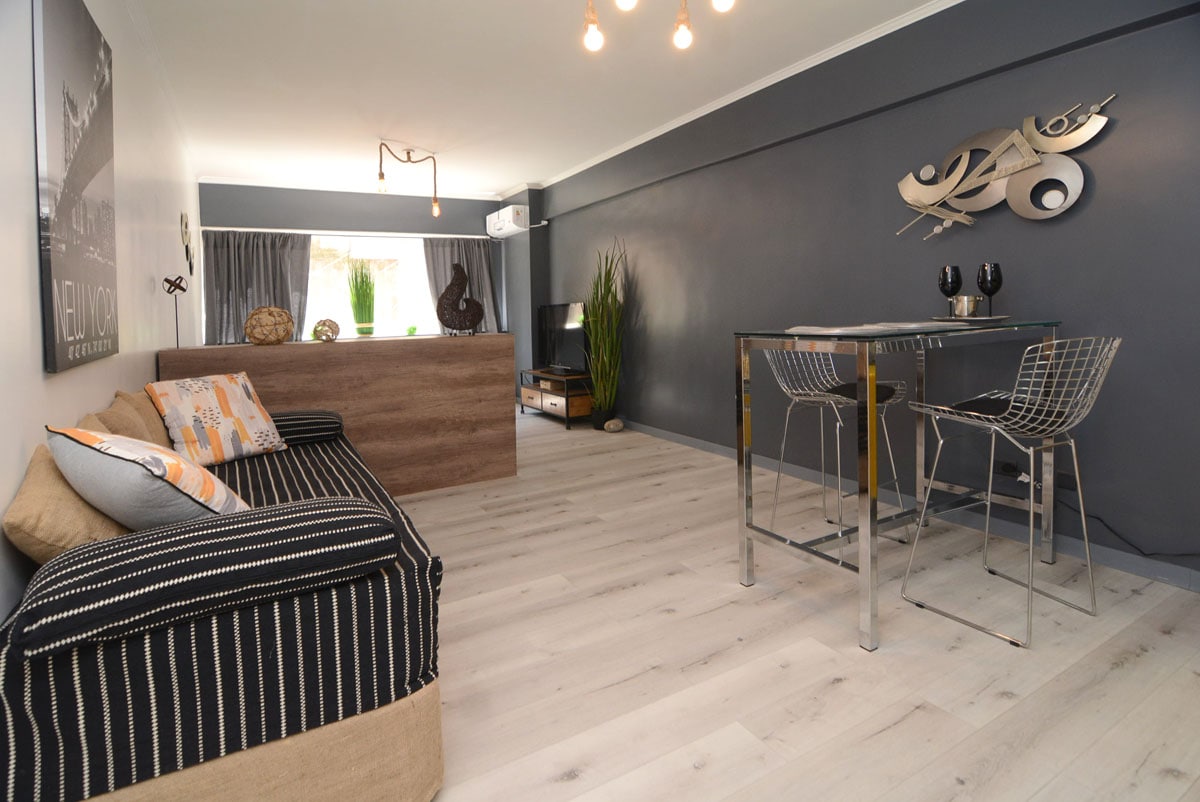 An open living space features a comfortable couch with striped upholstery, accompanied by decorative cushions. A sleek dining table with clear chairs is positioned nearby, and a modern wall decor piece adds character. Natural light is welcomed through large windows, enhancing the airy feel.