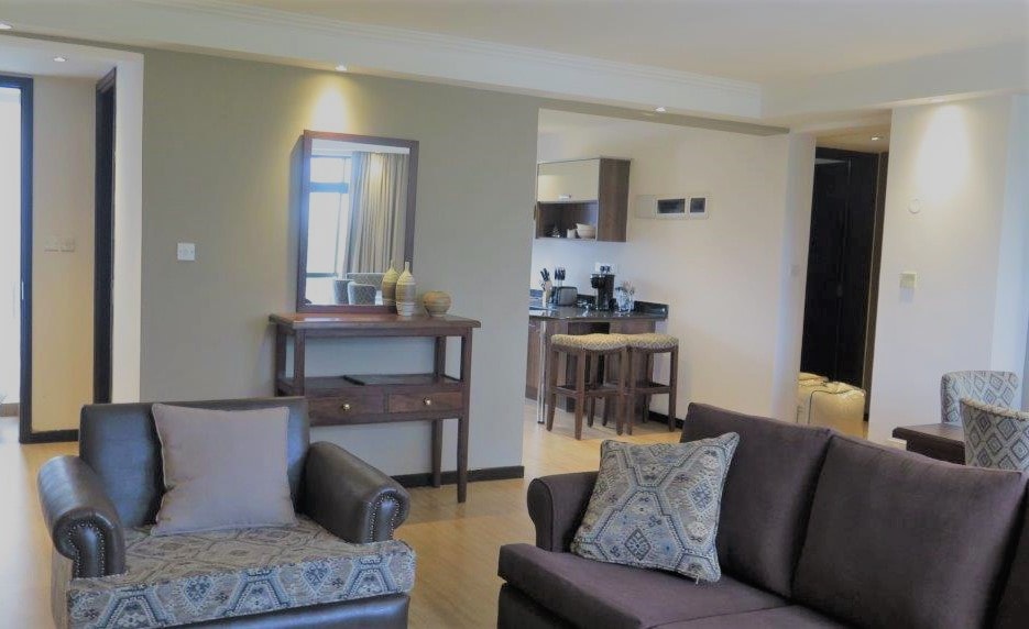 A modern living area features comfortable sofas and a decorative console table. The open plan layout connects the lounge to the kitchen, enhancing the spacious feel. Natural light filters in through large windows, while neutral tones create a calming ambience throughout the space.