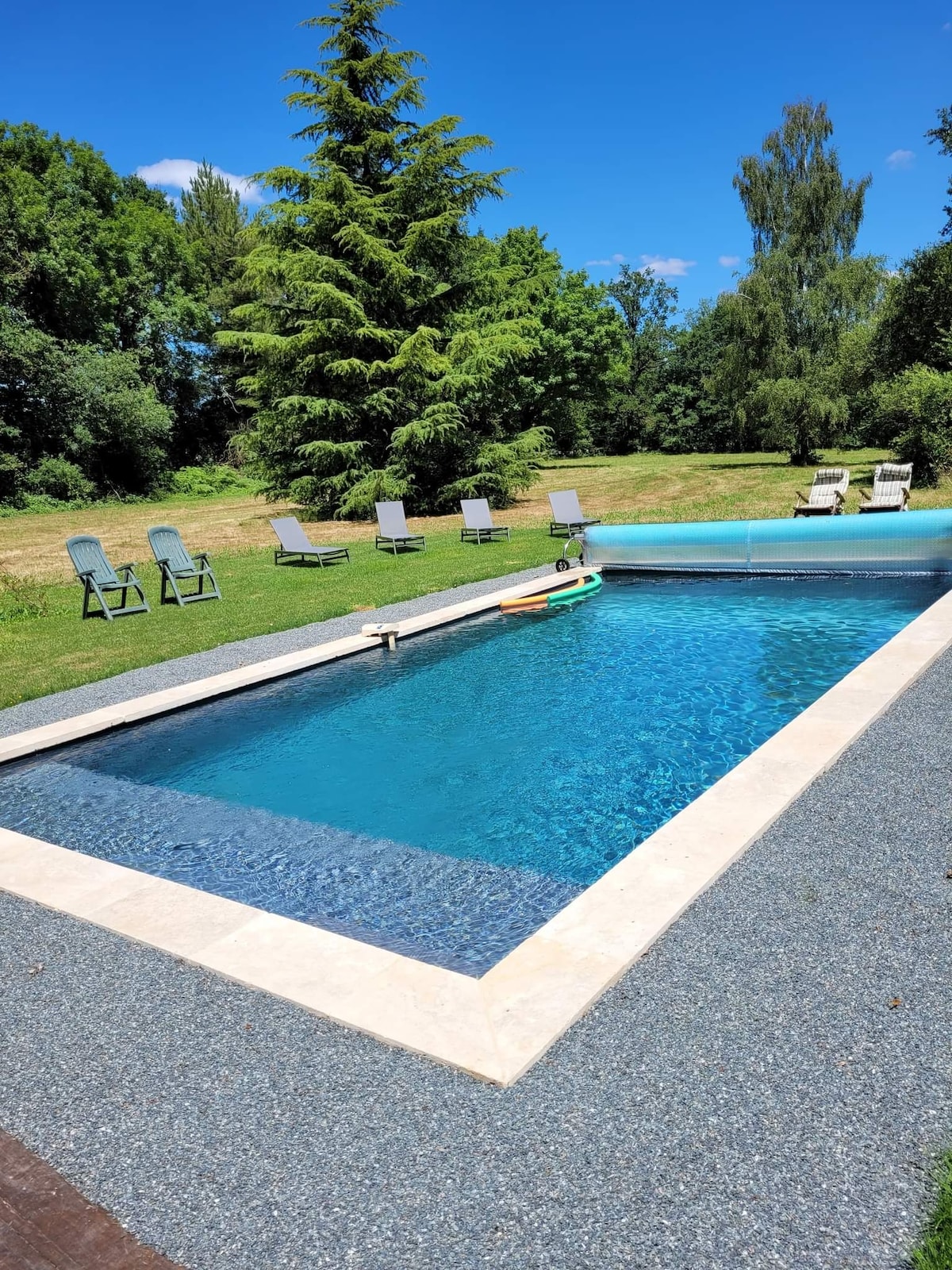 A serene swimming pool is surrounded by well-kept grass, inviting relaxation. Several lounge chairs are arranged nearby, providing seating options in the sun. Lush trees and greenery form a natural backdrop, enhancing the tranquil setting.