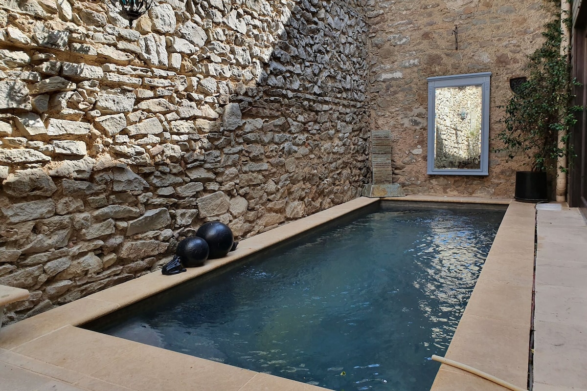 A private swimming pool is set within a beautifully restored stone barn. The pool area features smooth stone walls, a large mirror reflecting the natural light, and a couple of black exercise balls resting nearby, creating a serene atmosphere for relaxation.