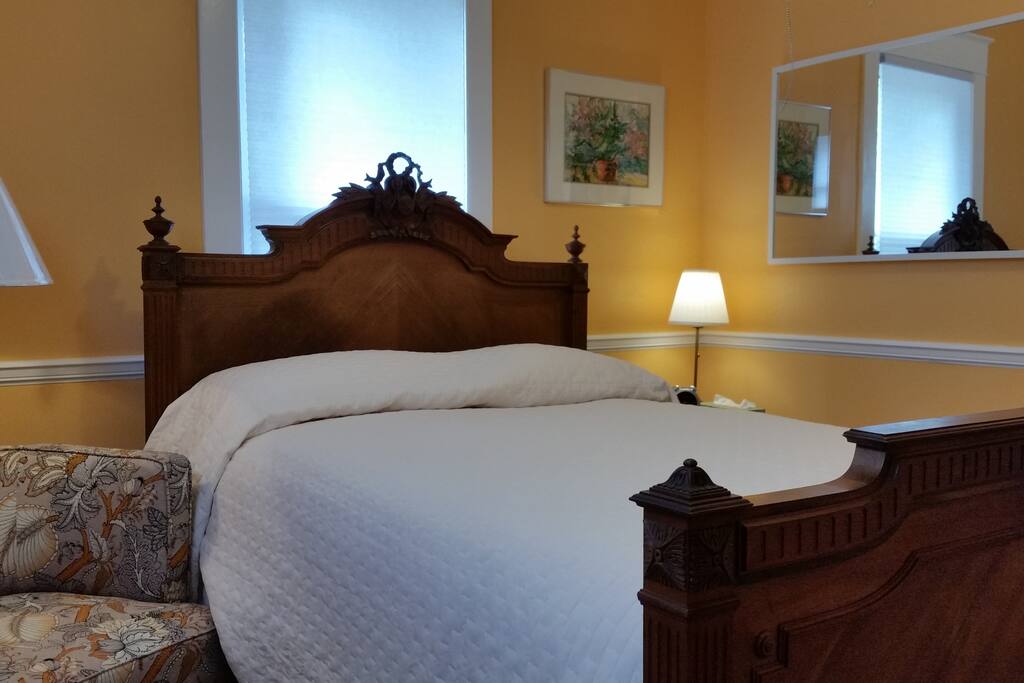 Bright bedroom with reading chair, desk, closet with luggage rack and room darkening shades.