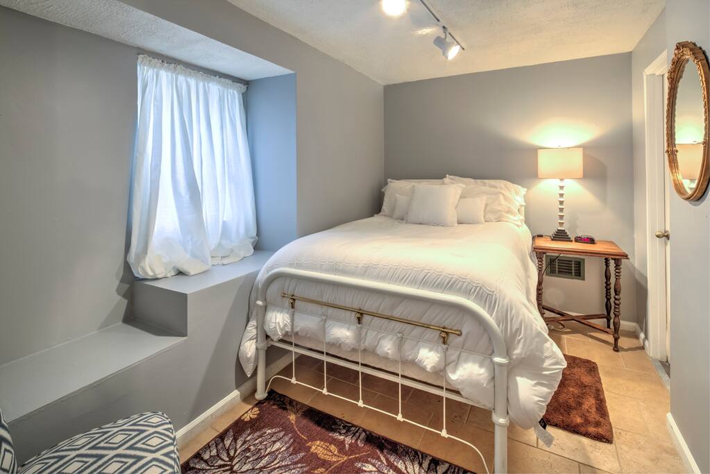 Cozy bedroom including full-length mirror, alarm clock, luggage rack, closet, hangers, iron, and comfortable chair