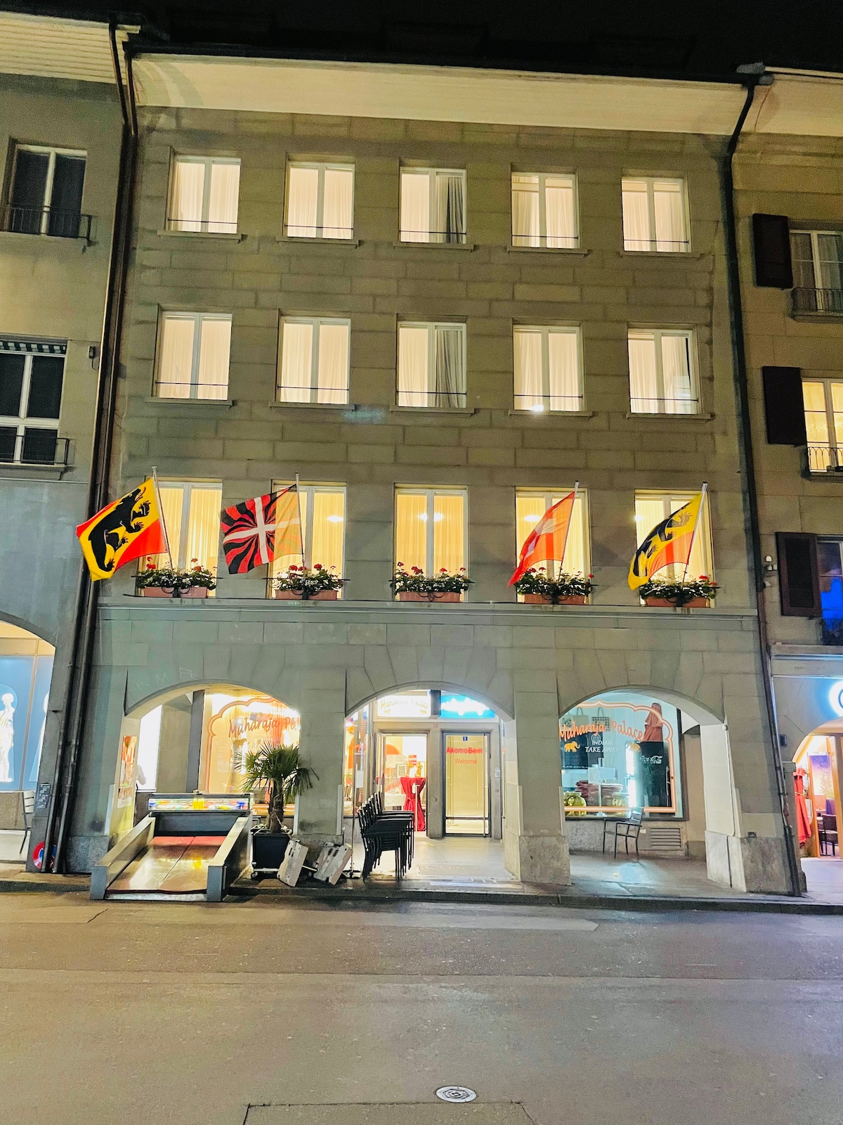 The exterior view of the building showcases a classic architectural style with large windows adorned by flower boxes. Flags are displayed prominently, enhancing the façade. The entrance is highlighted, offering a warm welcome to guests approaching from the street.