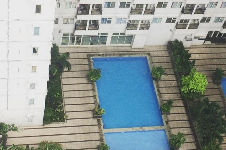 Two swimming pools are visible within a courtyard, surrounded by neatly arranged tiled paths and greenery. The pools are filled with clear blue water, reflecting the surrounding architecture and plant life.