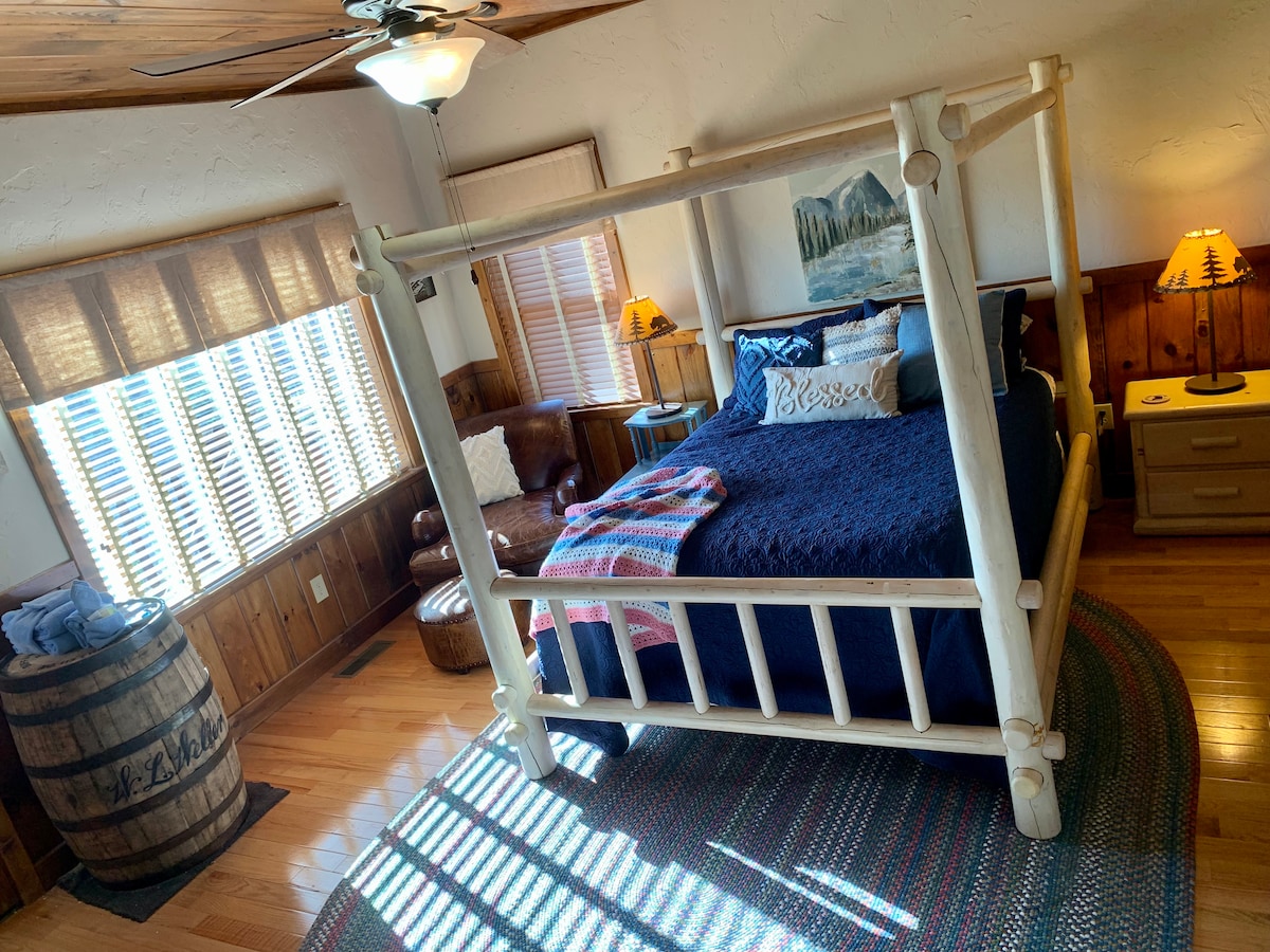 Bedroom 2, located on the main, includes a comfy queen bed with pillow-top mattress and mountain views! Enjoy a good book from the leather chair and ottoman. This room also has a private entrance to the deck. 