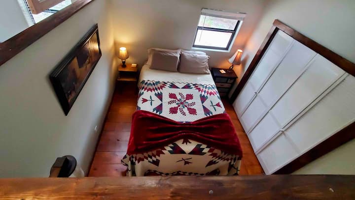 Bird’s eye view of the upstairs bedroom: There is a comfy queen bed and the privacy wall is open at the top to allow natural light to pour in (as well as a view of the ever-changing sky through the high windows). A full futon is located in the den. 