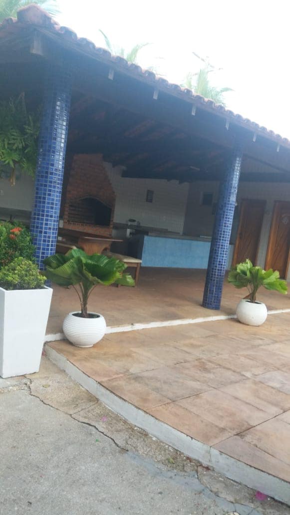An outdoor kitchen area is framed by blue-tiled columns, featuring a brick oven and a sleek countertop. Potted plants add a touch of greenery to the space, which is adorned with a tiled floor and surrounded by walls that enhance the open-air atmosphere.