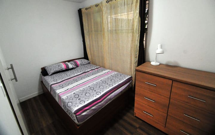 Chumba chenye starehe kwenye ghorofa ya kwanza, kilicho na kitanda kamili, kabati la kuhifadhia, bafu la kujitegemea, madirisha yasiyopenyeza sauti, mapazia ya kuzima mwanga kwa ajili ya mapumziko bora, meza ya usiku na feni kwa ajili ya starehe.