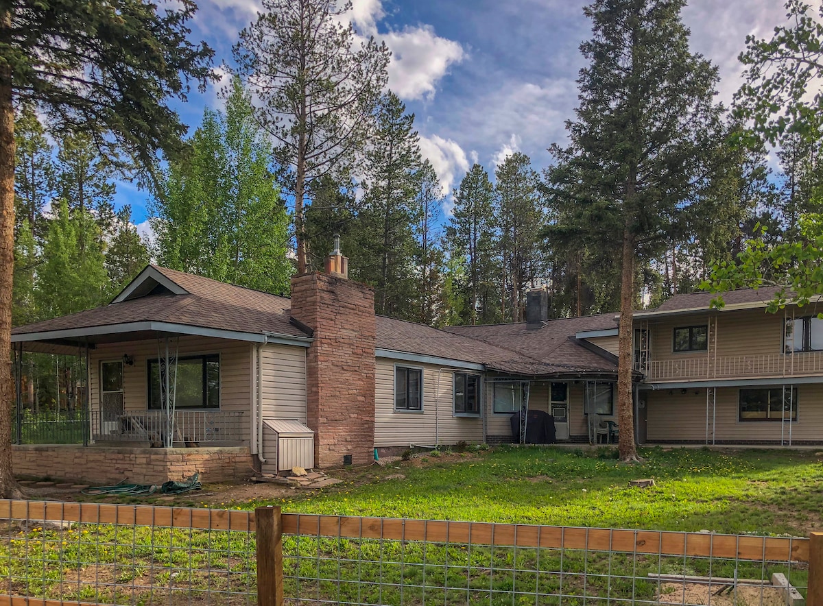 A spacious single-story home is highlighted within a natural setting, featuring a large fenced yard bordered by trees. The exterior includes a stone chimney and a covered porch area, offering a welcoming retreat for outdoor relaxation.