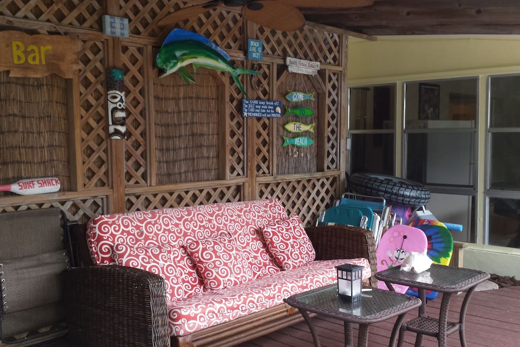 Covered patio area with fun tiki style decor, ceiling fan, lounging, and seating.