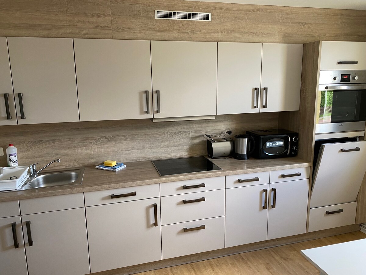 A modern kitchen area features streamlined cabinetry in neutral tones, showcasing built-in appliances including a microwave and oven. A countertop is equipped with a sink and stove, while a variety of kitchen tools are neatly arranged for convenience.