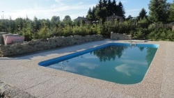 An outdoor swimming pool is situated within a landscaped area, surrounded by natural elements. The pool has a clear blue water surface and is enclosed by a stone border, providing a serene atmosphere for relaxation.
