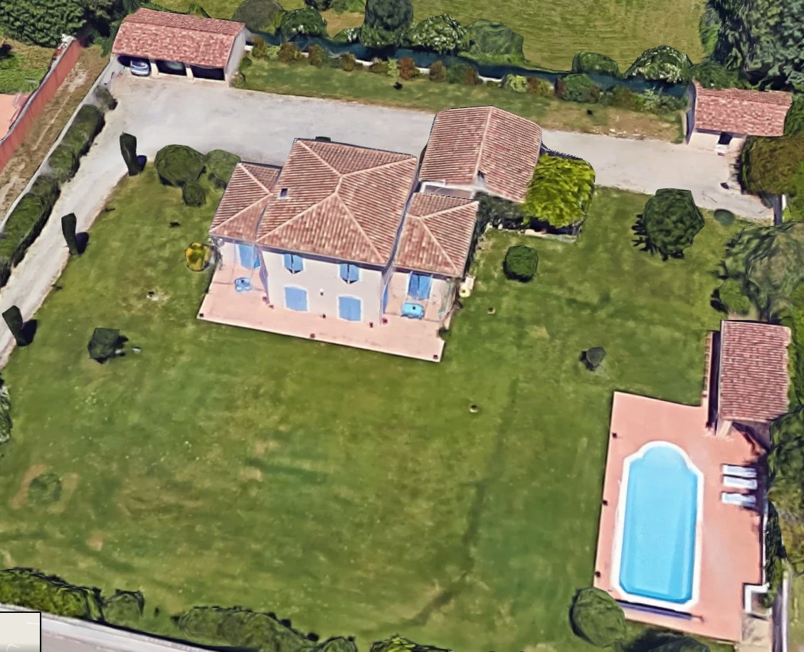 The villa is situated in a spacious green landscape, featuring a well-maintained garden surrounding a private pool. The building showcases a traditional Provençal design with a tiled roof and multiple outdoor seating areas for relaxation.