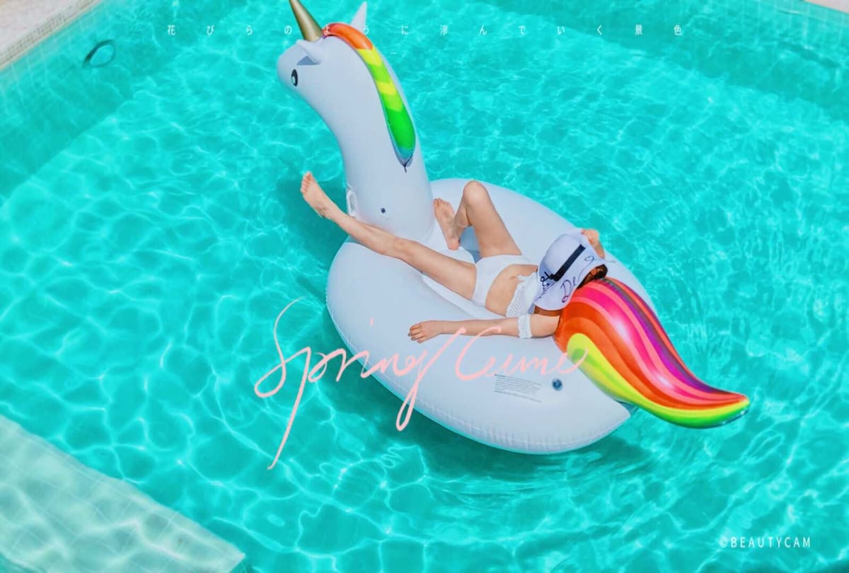 A large inflatable unicorn floats in a swimming pool, surrounded by clear turquoise water. The unicorn features a rainbow mane and colorful tail. Sunlight reflects off the water, creating a serene and inviting atmosphere around the pool area.